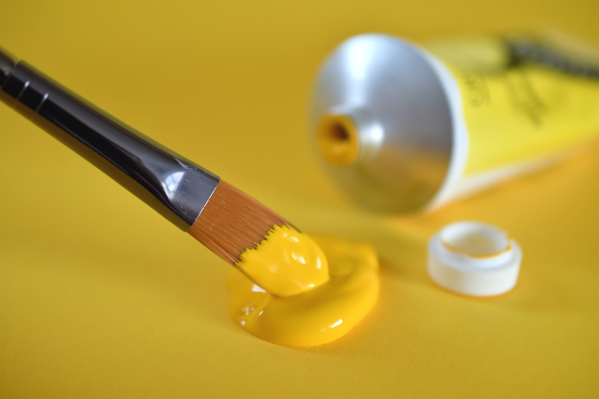 A paintbrush dipping into yellow paint with an open tube of yellow paint, hobby, hobbies