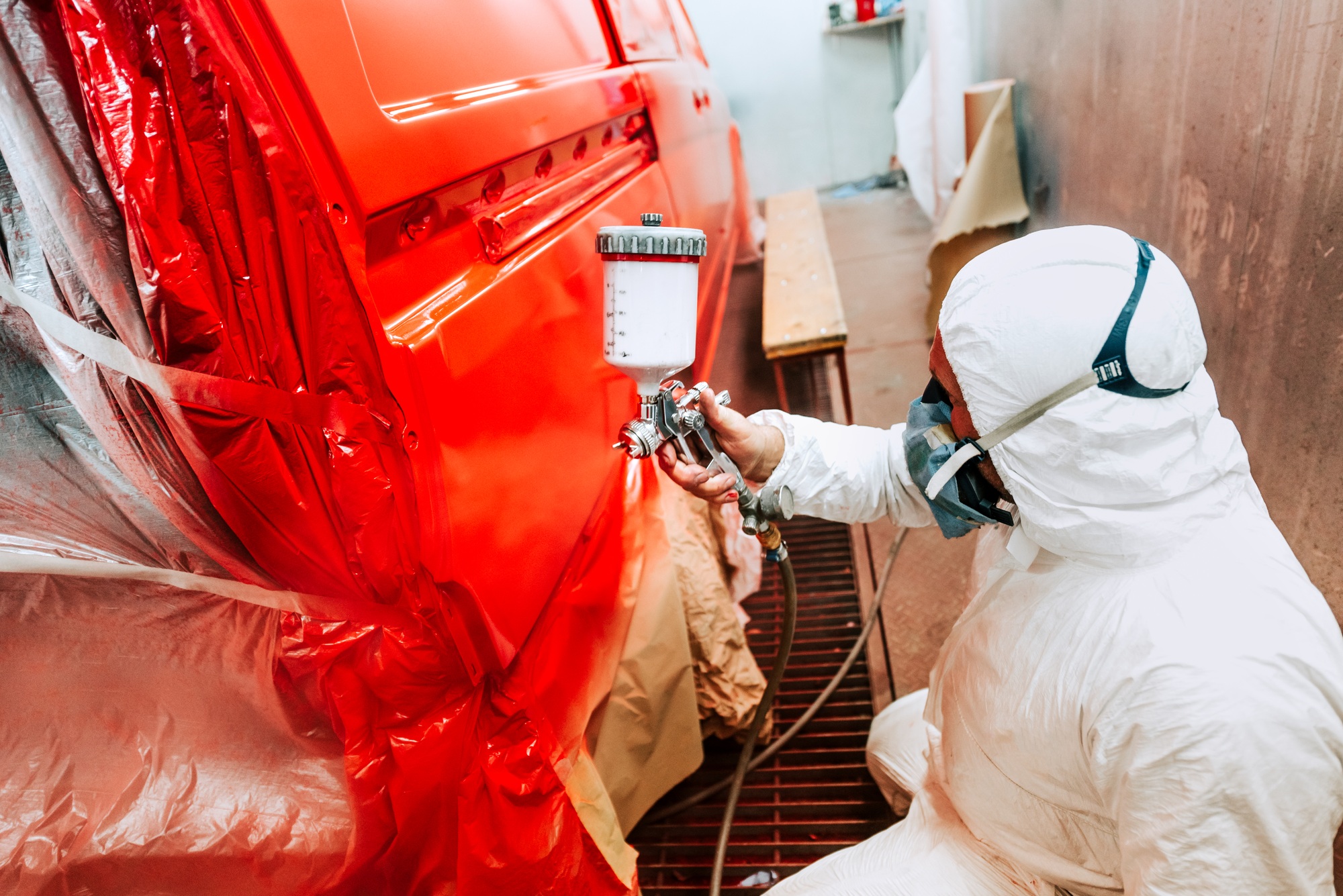 Painter working and painting a red car in paint garage