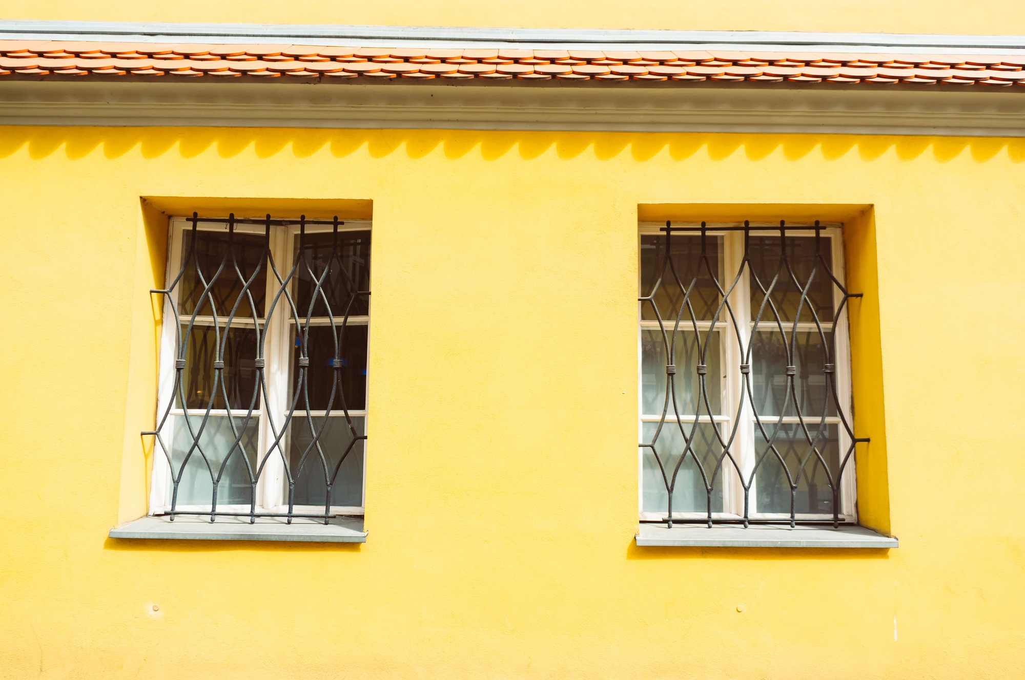 Two windows on a yellow building and a roof